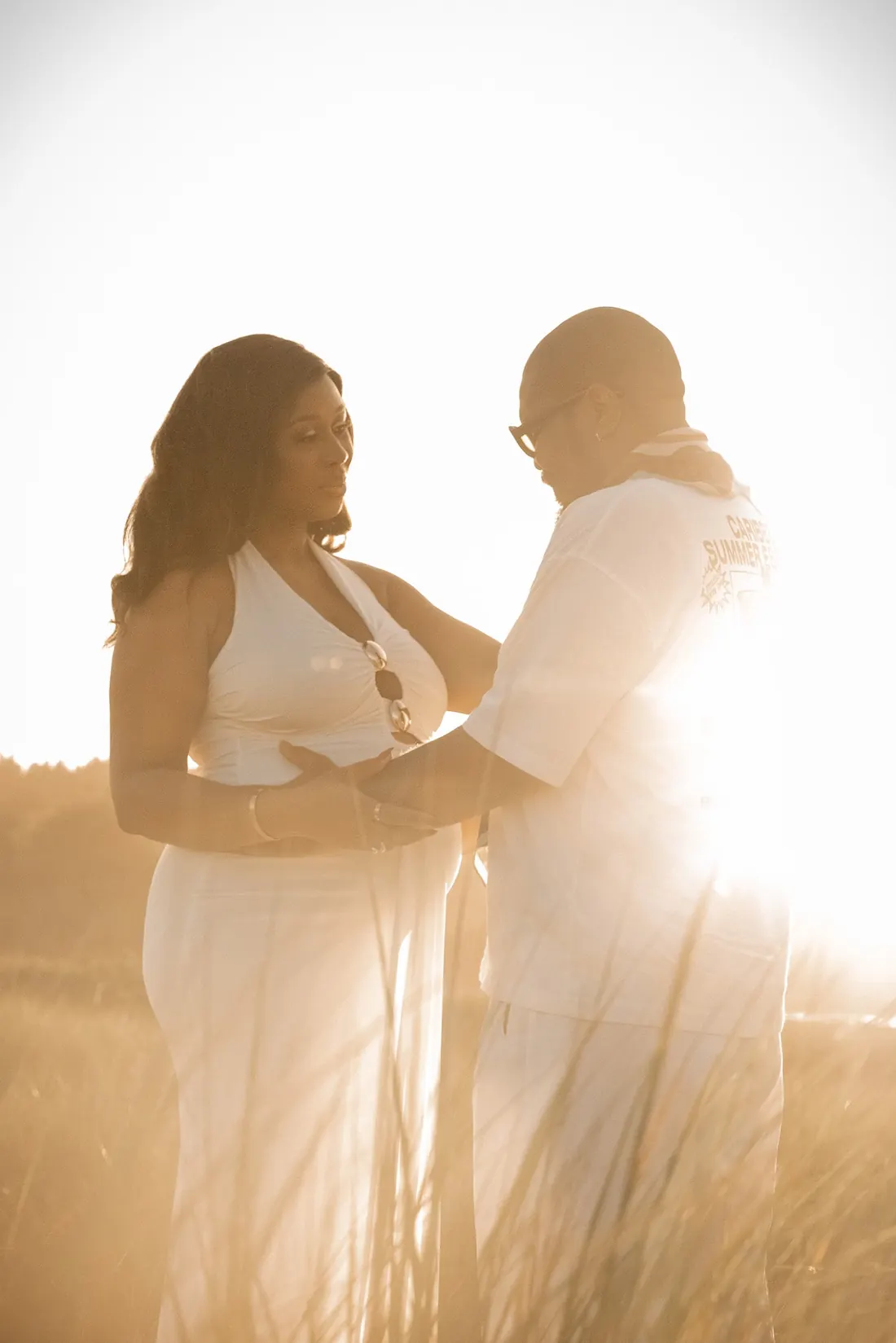 A couple facing each other in tall grass, backlit by low sun.