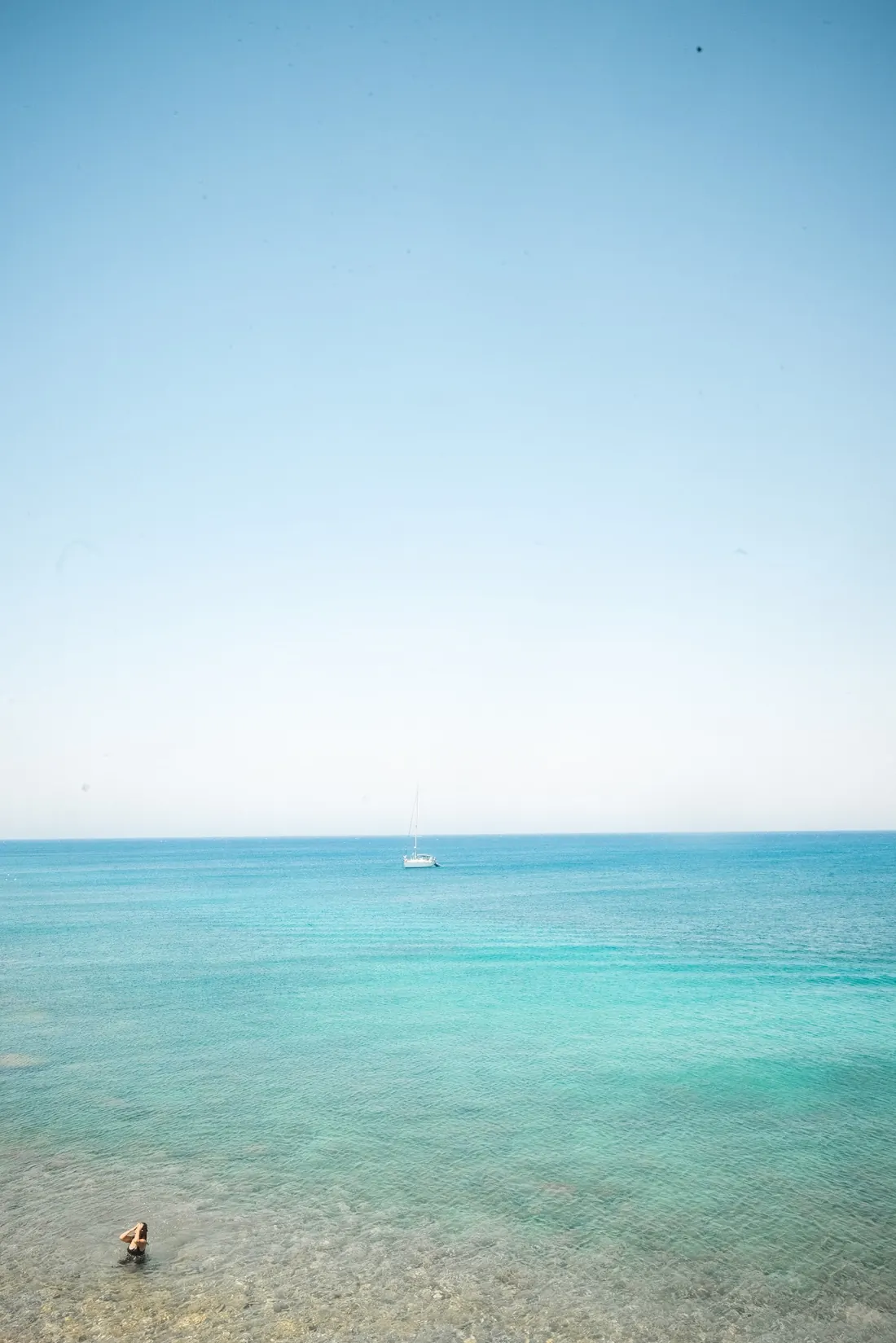 A single sailboat on open turquoise water.