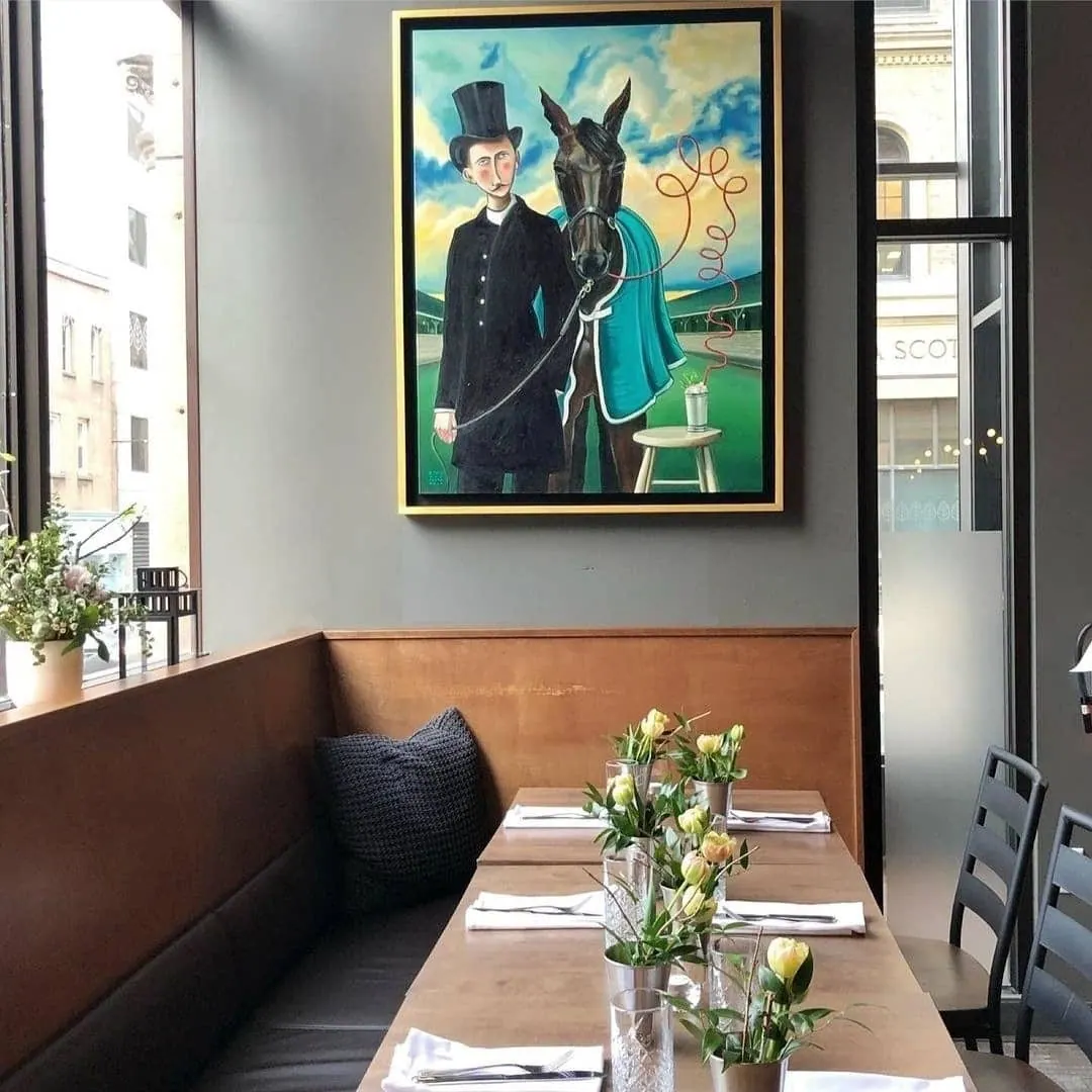 Large framed painting of a figure in a top hat beside a horse, hung above a restaurant banquette