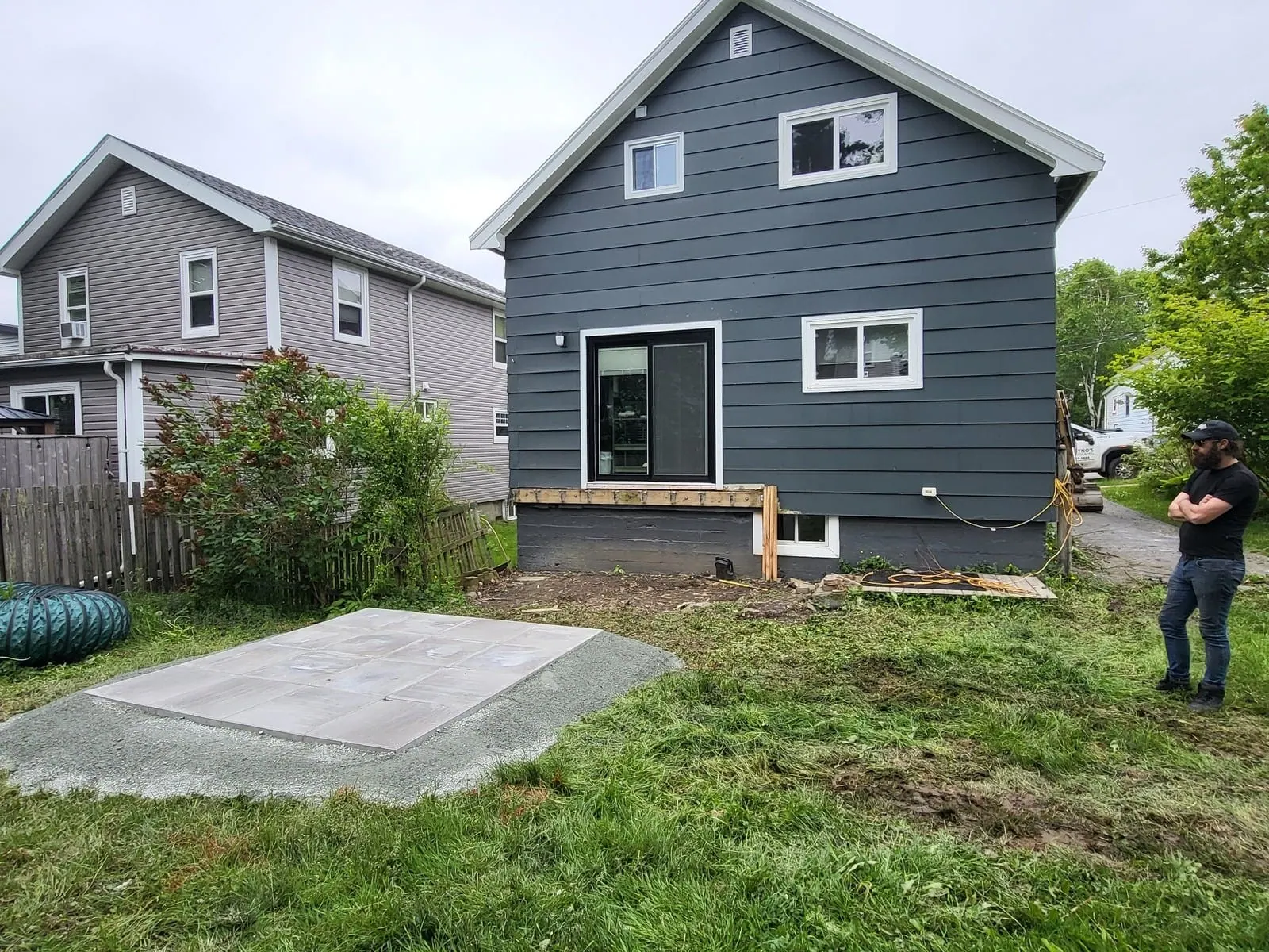 Back yard before: lawn and a concrete pad behind a dark blue house