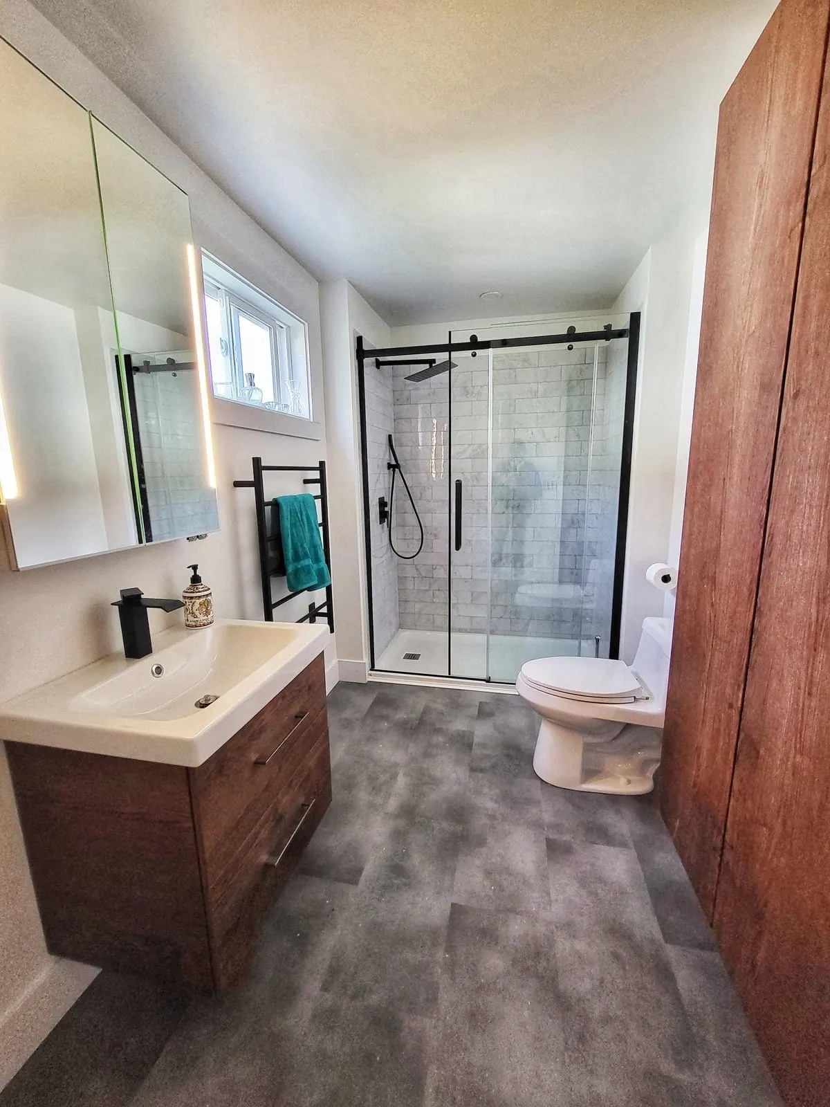 Renovated bathroom with a glass walk-in shower, floating wood vanity and grey plank floor
