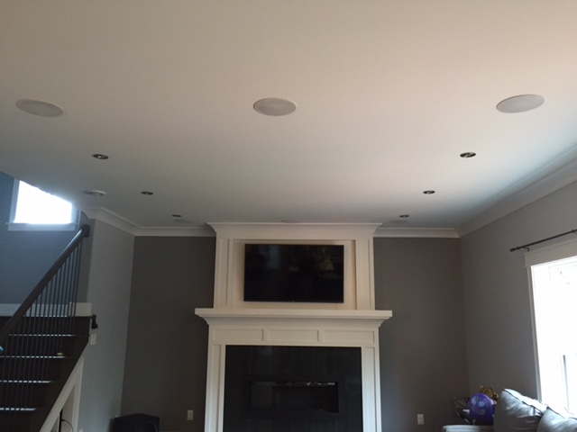 Living room ceiling with three flush-mounted speakers above a TV set into the mantel