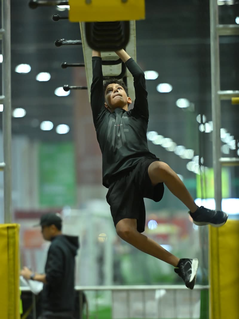 A competitor swinging between hanging holds on the yellow ninja course