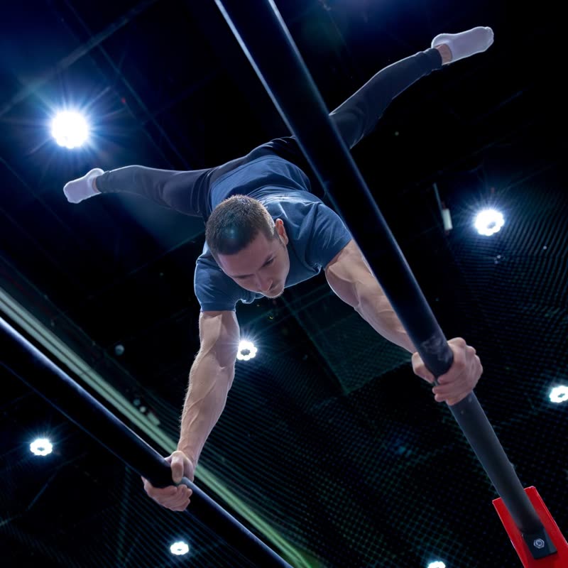 An athlete in a straddle hold on the bar under the arena lights