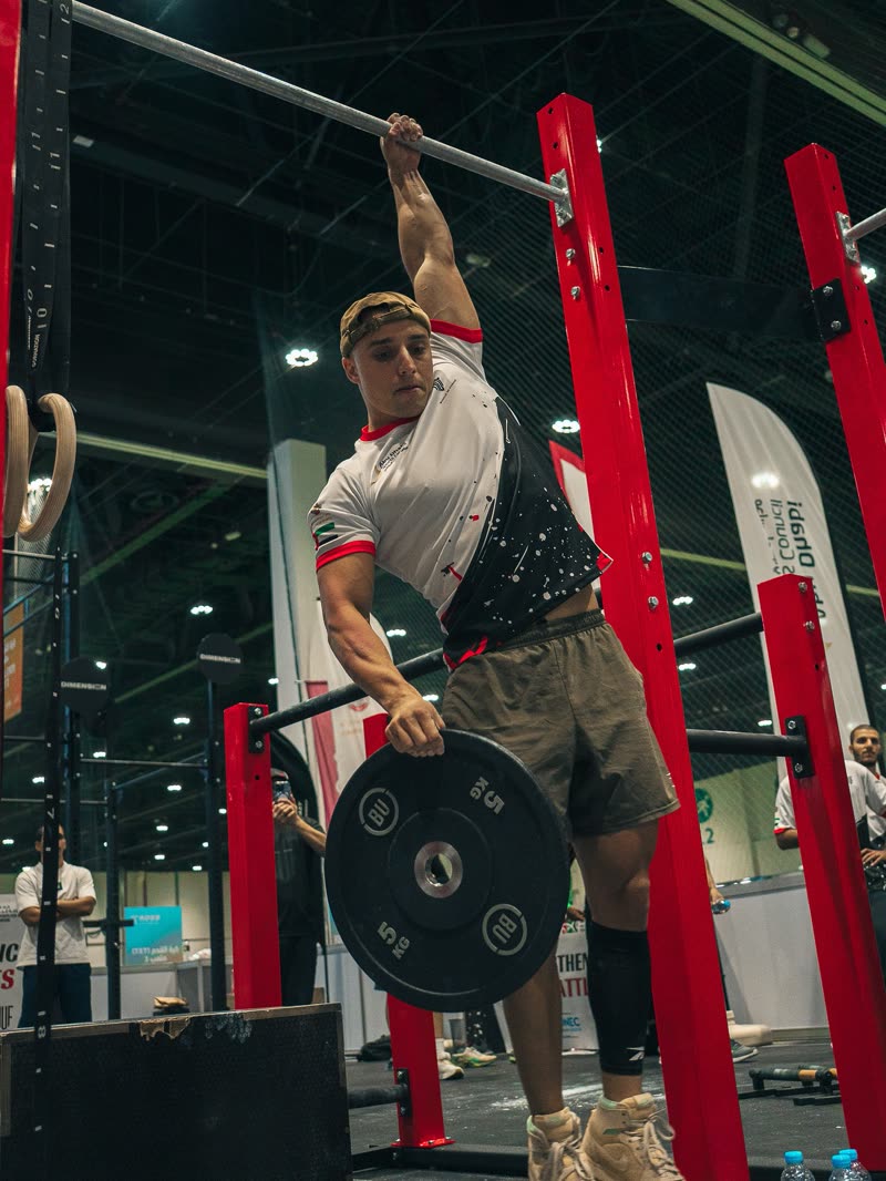 A competitor doing weighted pull-ups with a plate on a dip belt