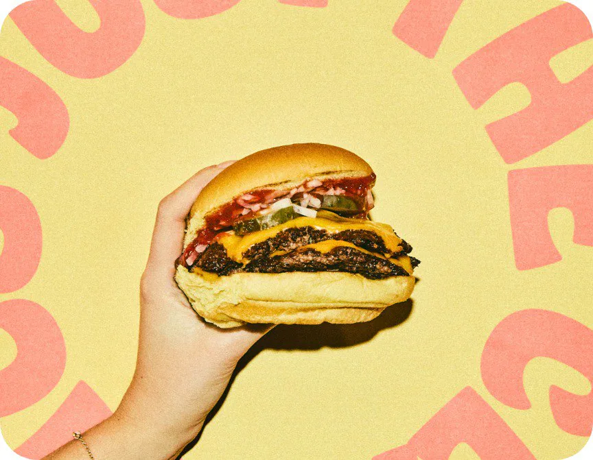 A hand holds up a Rosie's double smashburger against a yellow Rosie's backdrop