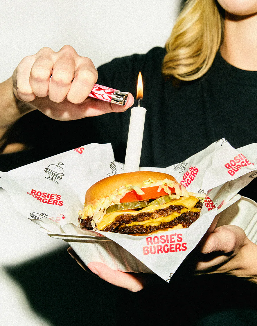 A Rosie's double smashburger held up with a birthday candle