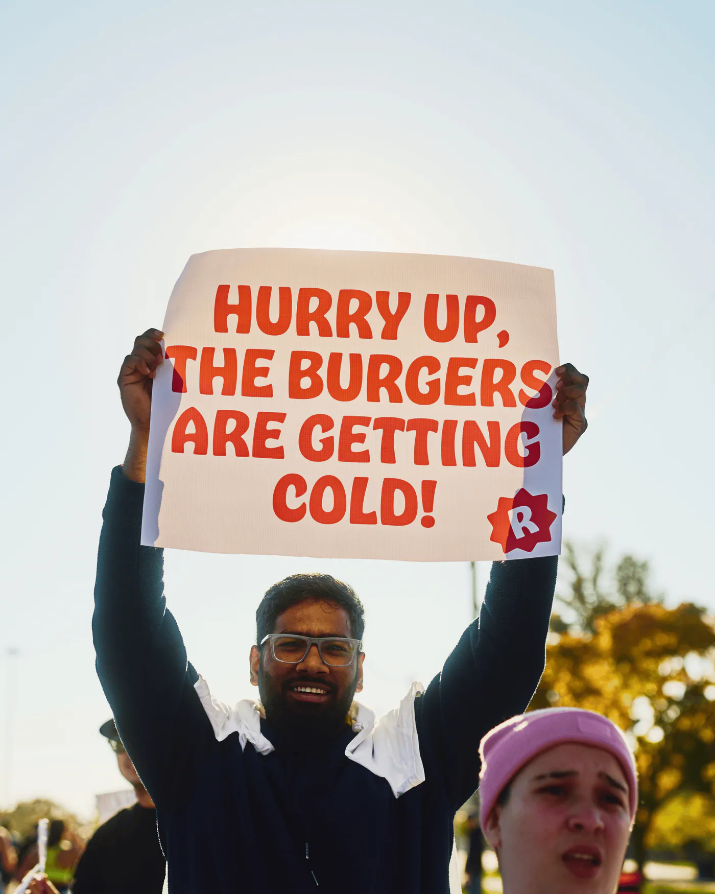 A spectator holds a sign reading Hurry up, the burgers are getting cold!