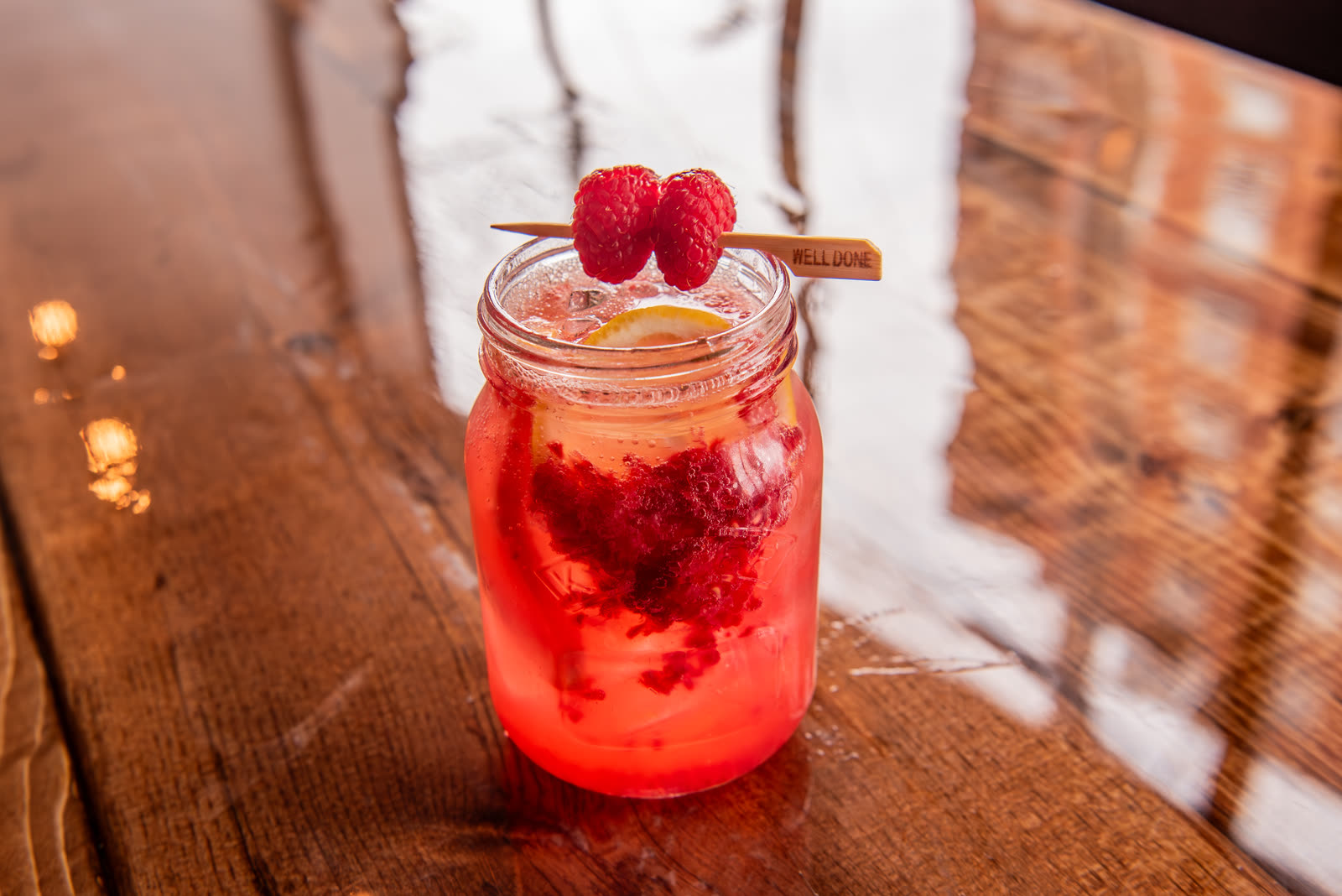 A raspberry citrus spritz in a mason jar on a wooden table